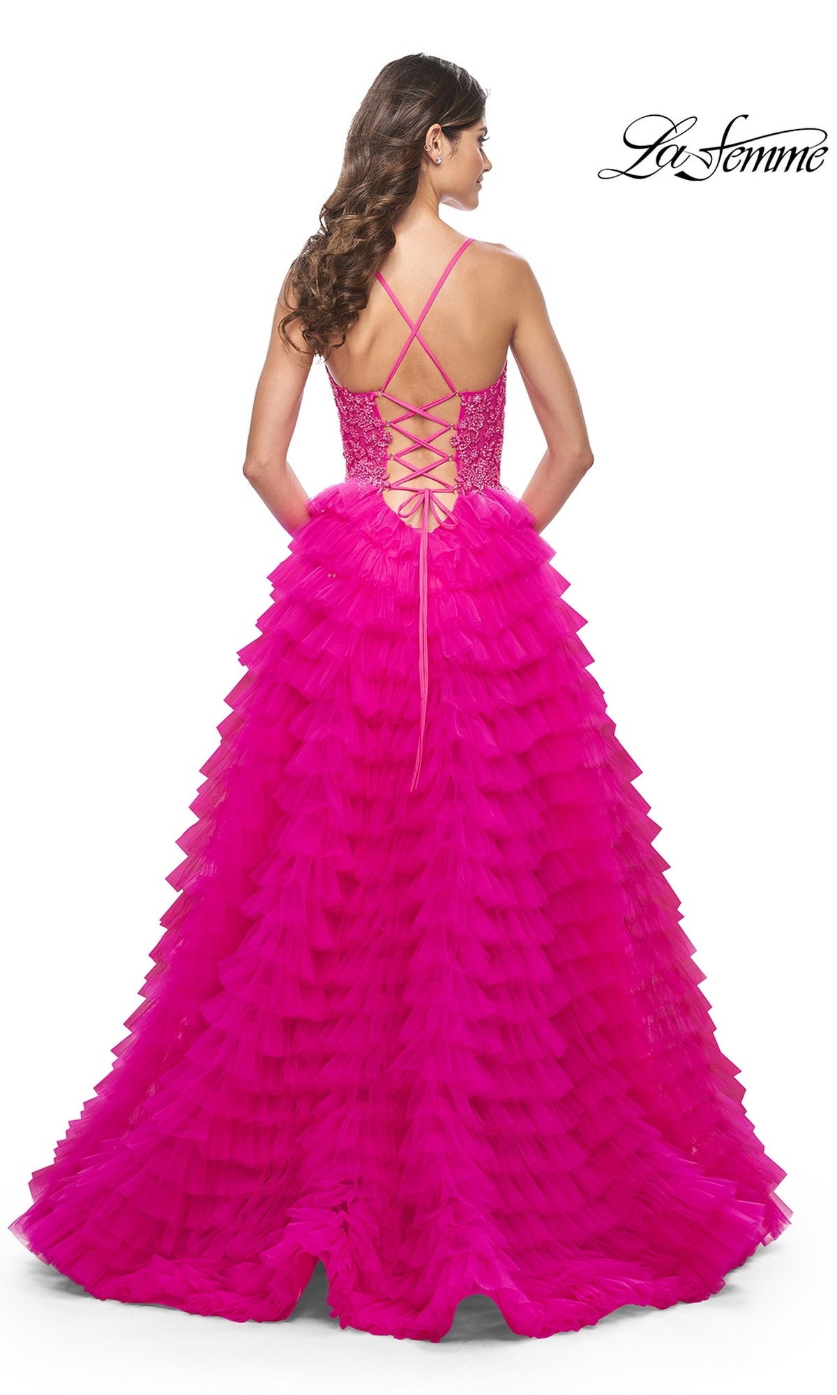 Woman wearing the La Femme Hot Pink Long Ruffled Prom Dress 32334, seen from behind. The gown has a lace-up back with criss-cross straps, an embroidered-lace bodice, and a full ruffled tulle skirt.